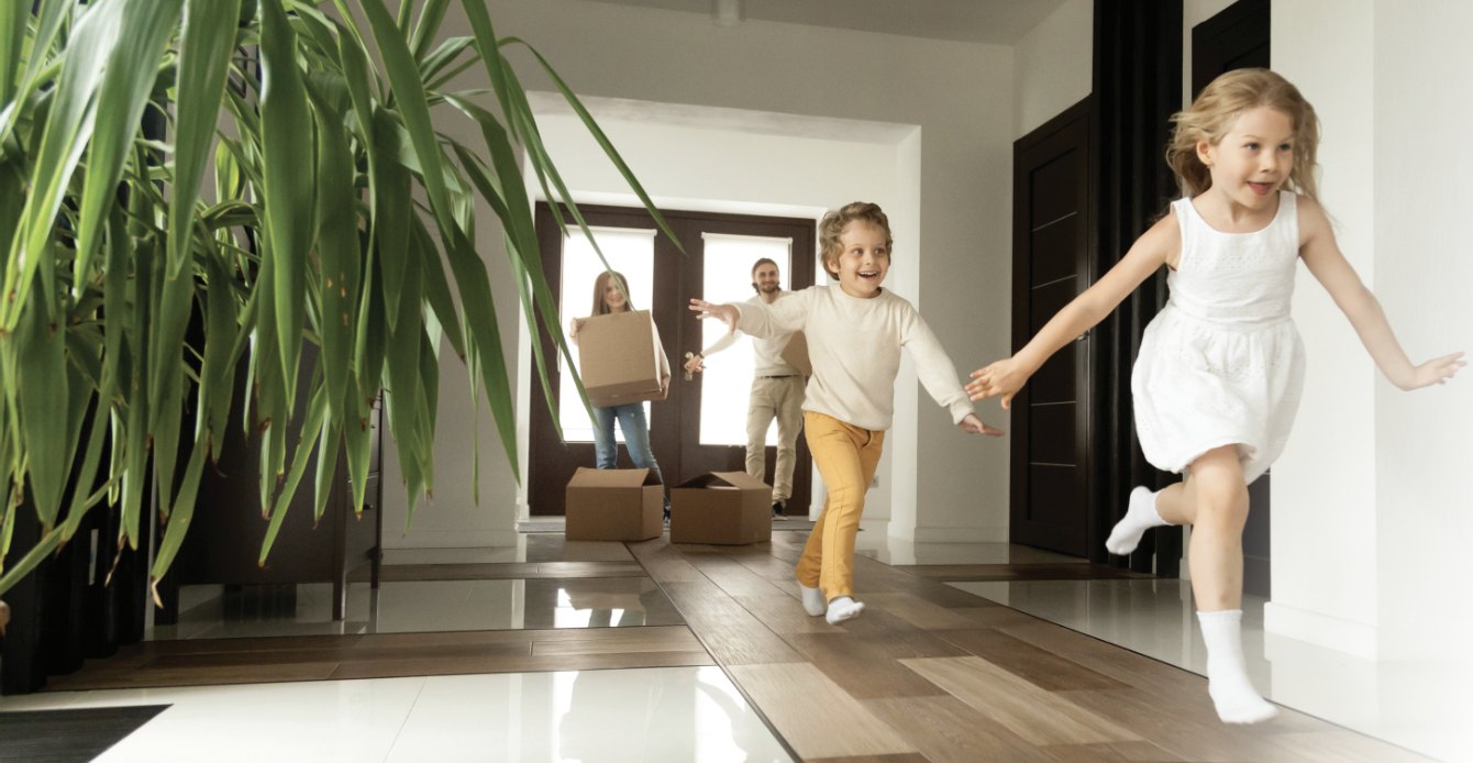 Children running into their family's new home while their parents carry in moving boxes